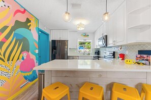 A kitchen with a large island, white cabinets, stainless steel appliances, and a colorful mural on the wall.