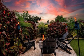 An outdoor seating area with chairs and a fire pit, surrounded by lush greenery and a sunset sky. - Happy Hacienda- Heated Pool, Hot Tub, Golf, Outdoor Games (Bradenton)