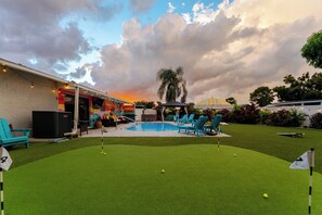 Quintal com piscina, grama sintética e área de varanda com móveis de exterior.