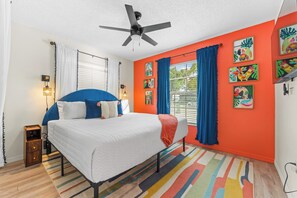 Una camera da letto con un letto, una ventola a soffitto, una finestra con tende e un tappeto colorato.