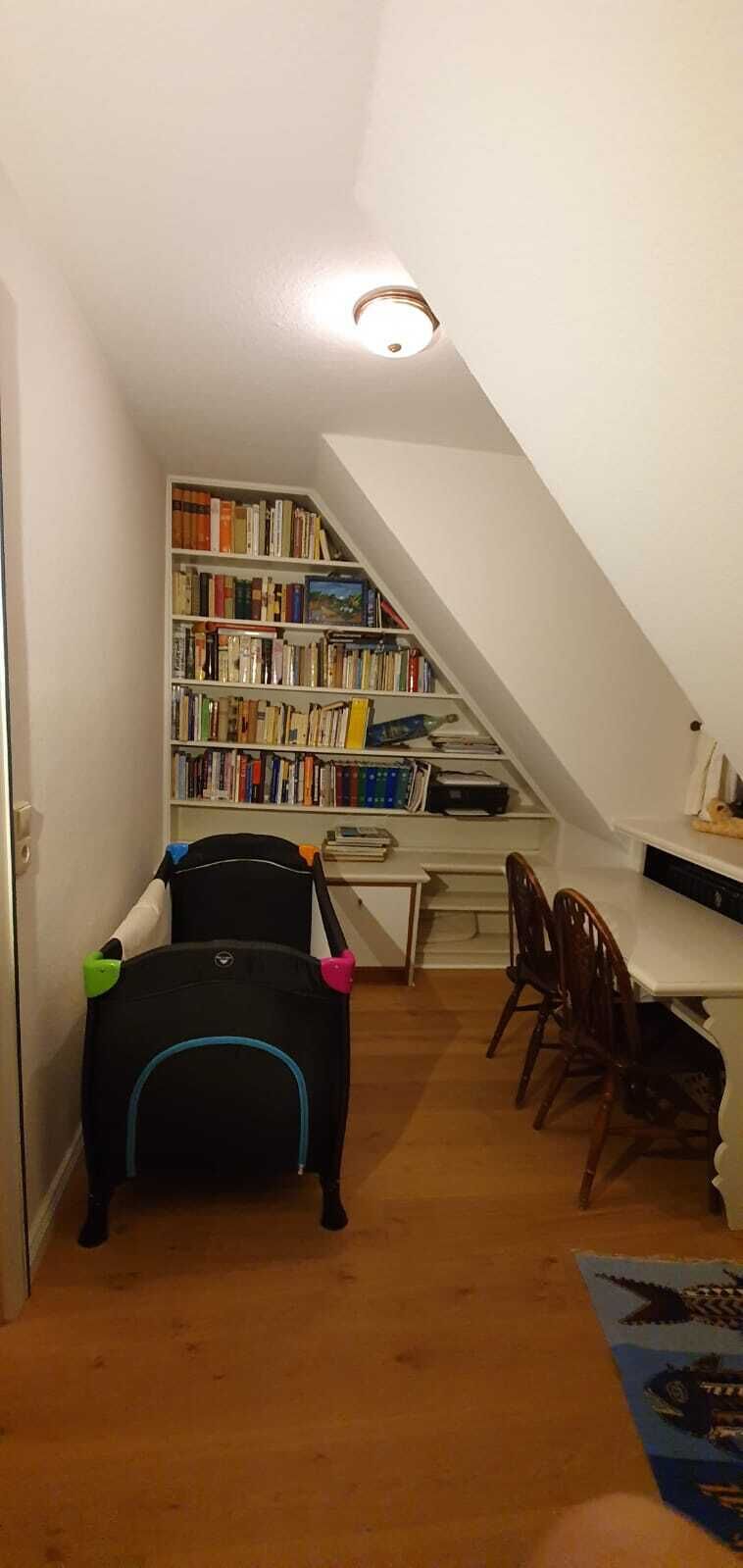 Une pièce avec une bibliothèque, un bureau, une chaise et une poussette.