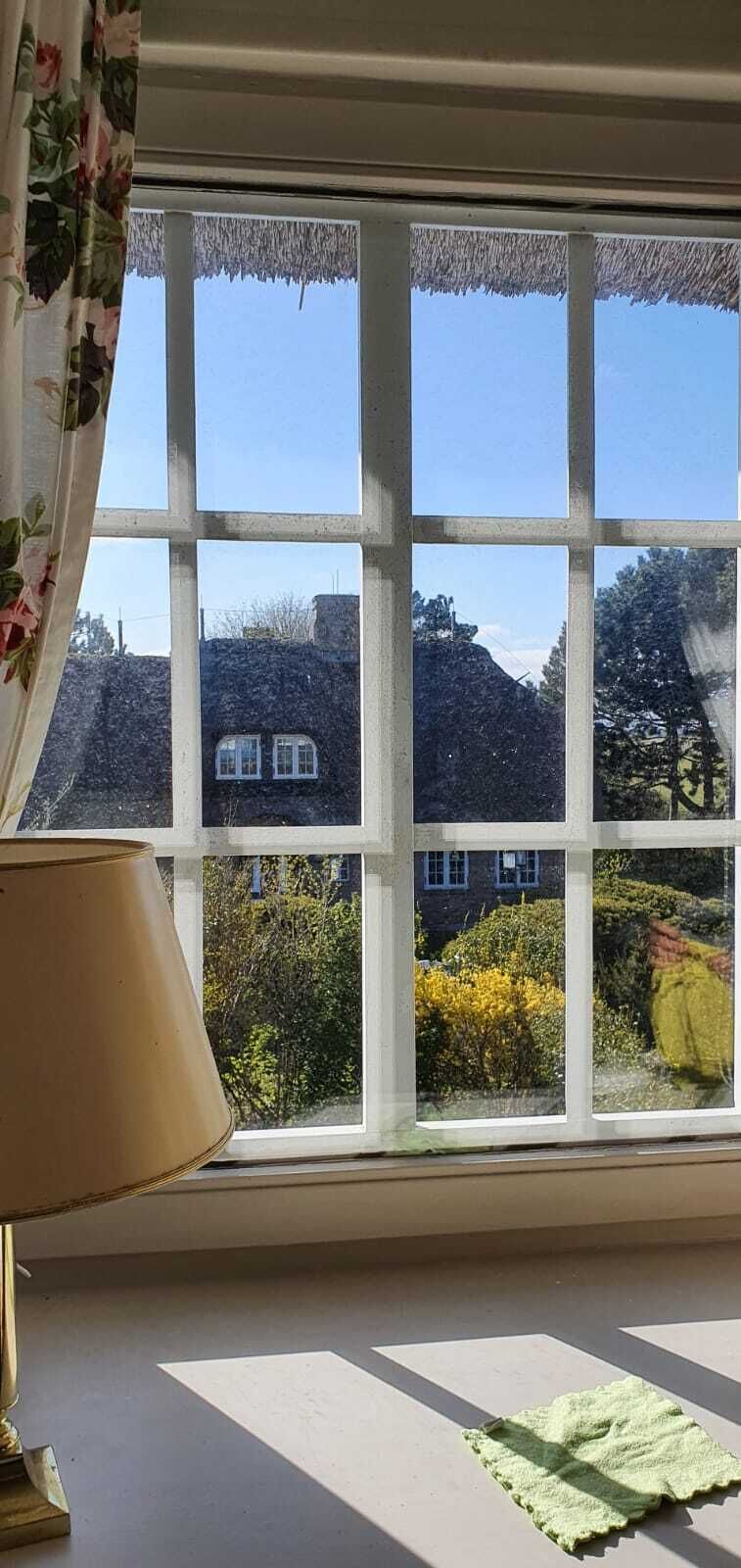 Ein Fenster mit Blick auf ein Steinhaus und Grünpflanzen.