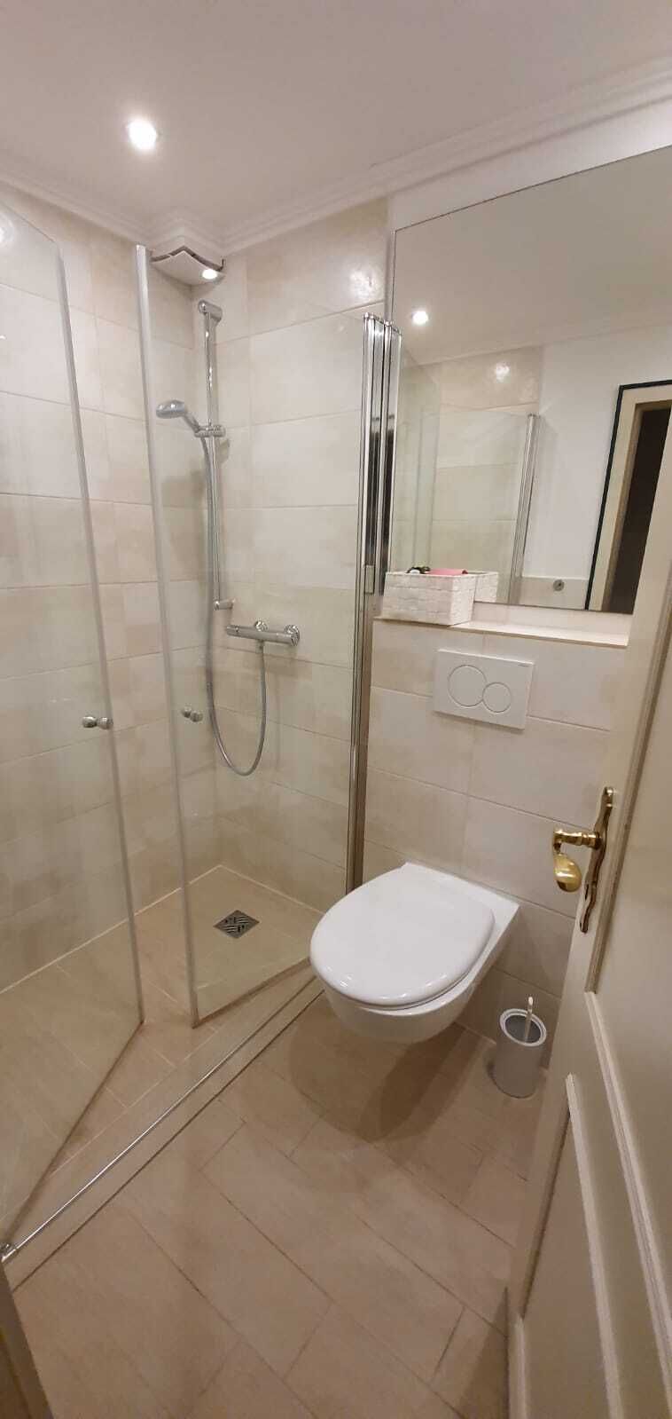 Une salle de bain moderne avec une douche à parois de verre, des toilettes blanches et un miroir au-dessus du lavabo.