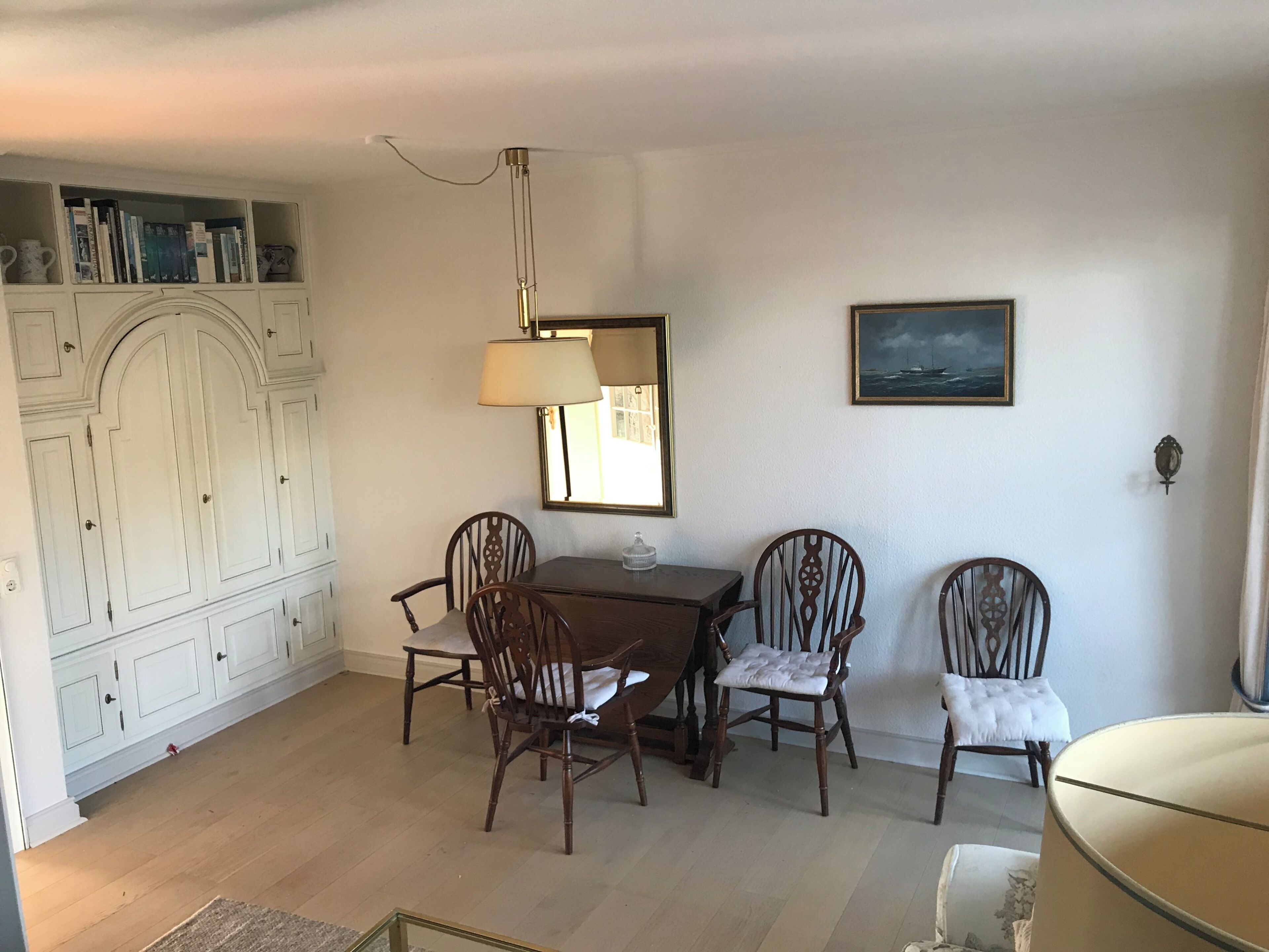 Ein Essbereich mit Tisch, Stühlen, einer Lampe, einem Spiegel und einem Bücherregal.