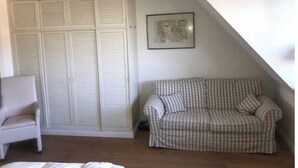 Ein Zimmer mit einem weißen Kleiderschrank, einem karierten Sofa, einem weißen Sessel und einem gerahmten Bild an der Wand.