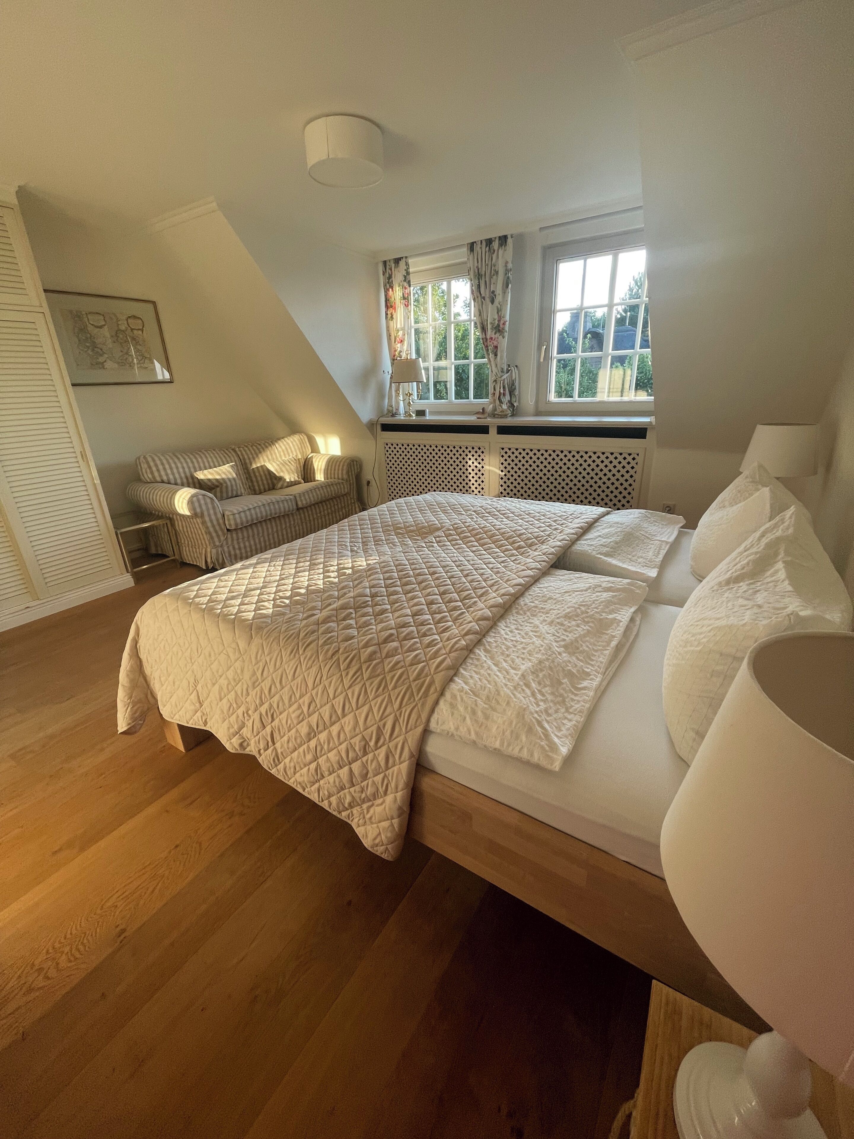 Ein Schlafzimmer mit einem Bett, einem Fenster mit Vorhängen, einem Heizkörper und einer Lampe.