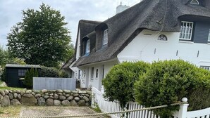 Ein traditionelles Haus mit einem steilen Satteldach, einer Steinwand und einem weißen Zaun.