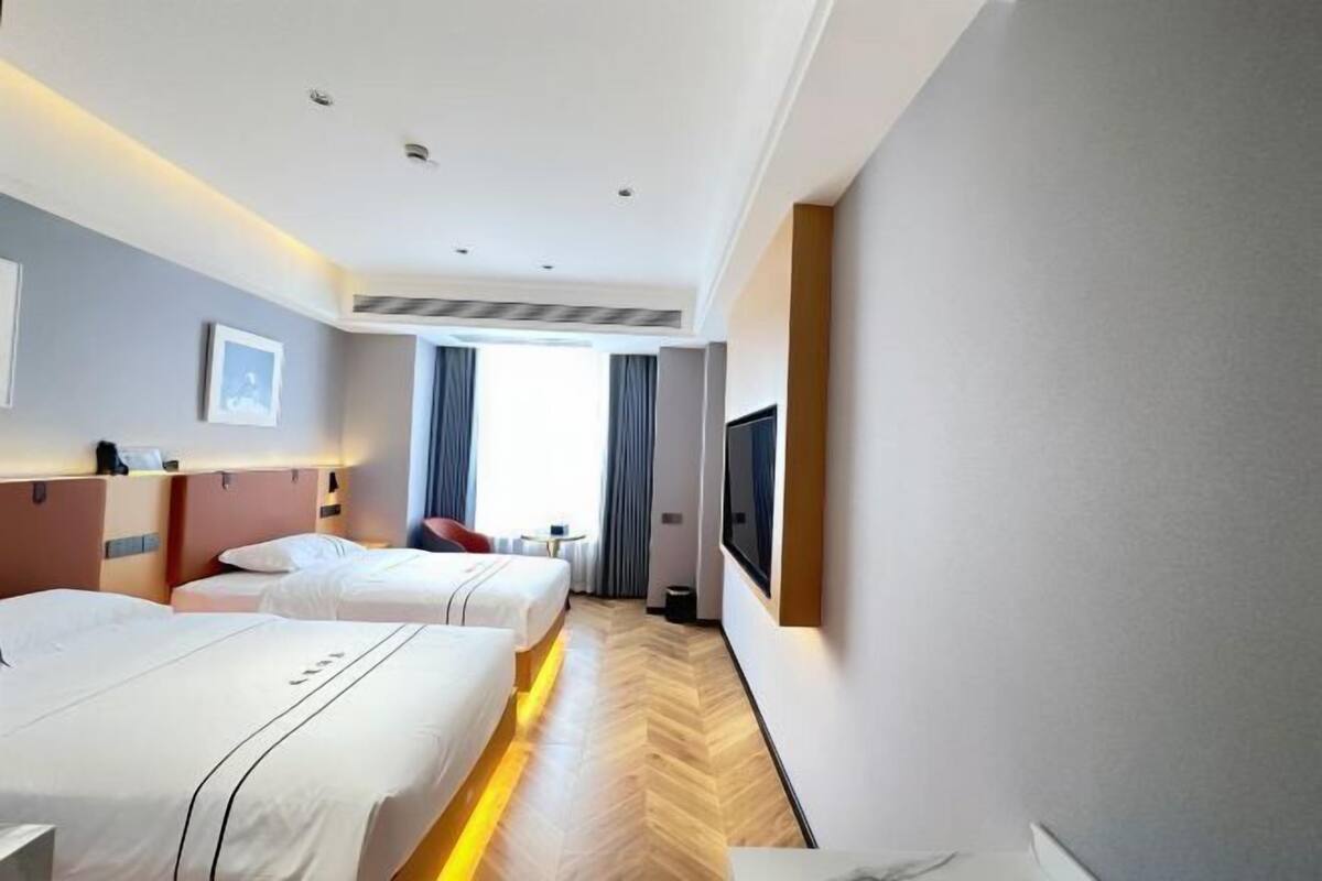 Habitación de hotel con dos camas, televisor, ventana con cortinas y suelo de madera.