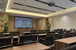 Une salle de conférence équipée d’un grand écran diffusant une présentation, de plusieurs tables et de chaises disposées pour les réunions.