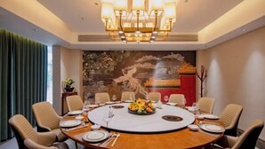A conference room with a round table, beige chairs, a chandelier, and a decorative wall.