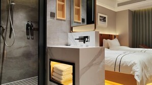 A hotel room with a shower, a mirror, a bed, and a built-in heater.