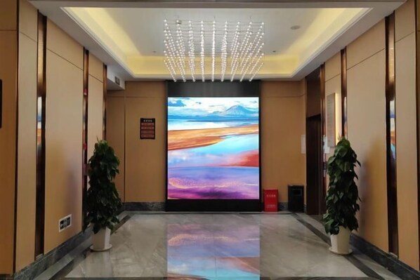 Un hall d’hôtel doté d’un grand écran numérique affichant un paysage, de plantes en pot et d’un luminaire moderne au plafond.