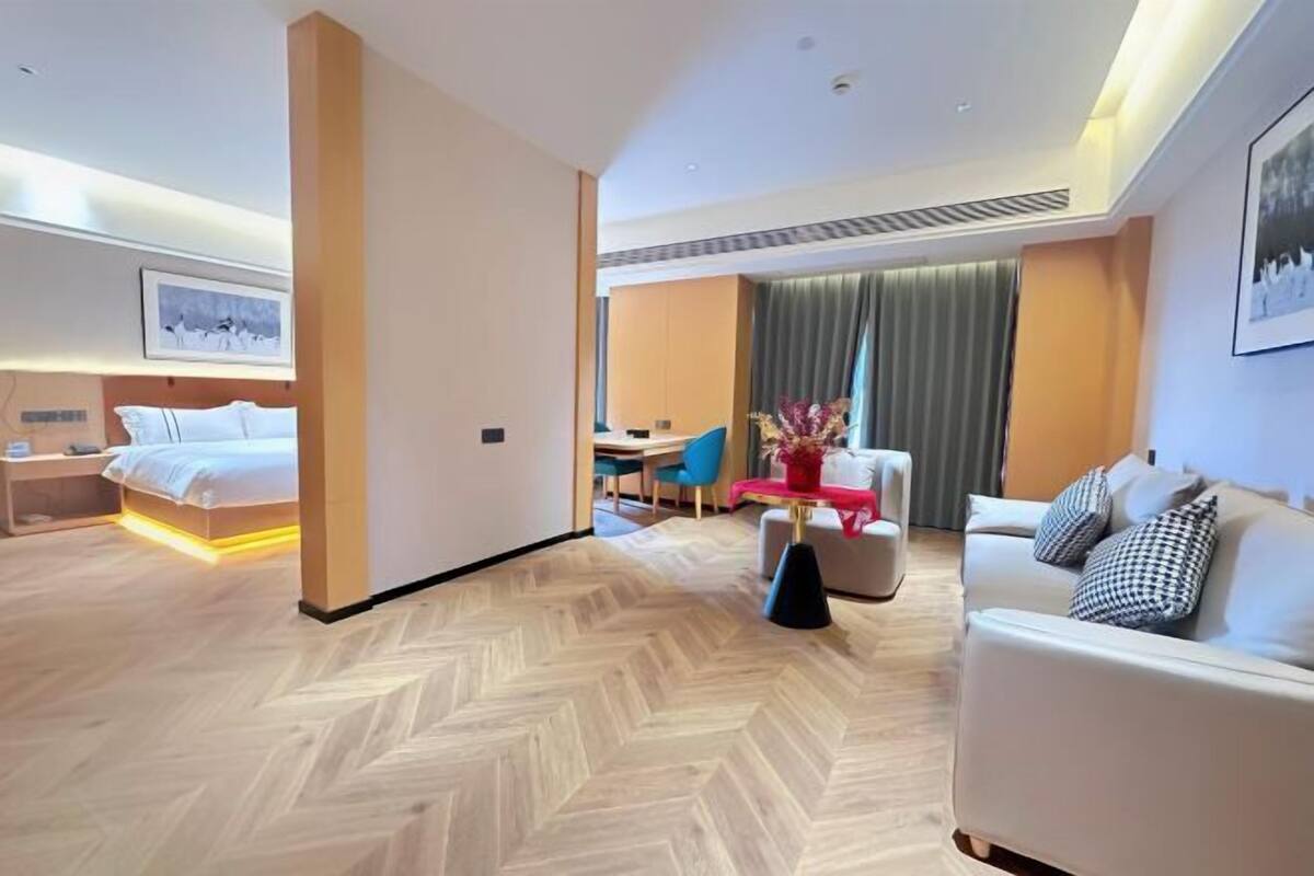 Una habitación de hotel con cama, sofá, mesa de comedor con sillas y un gran ventanal con cortinas.