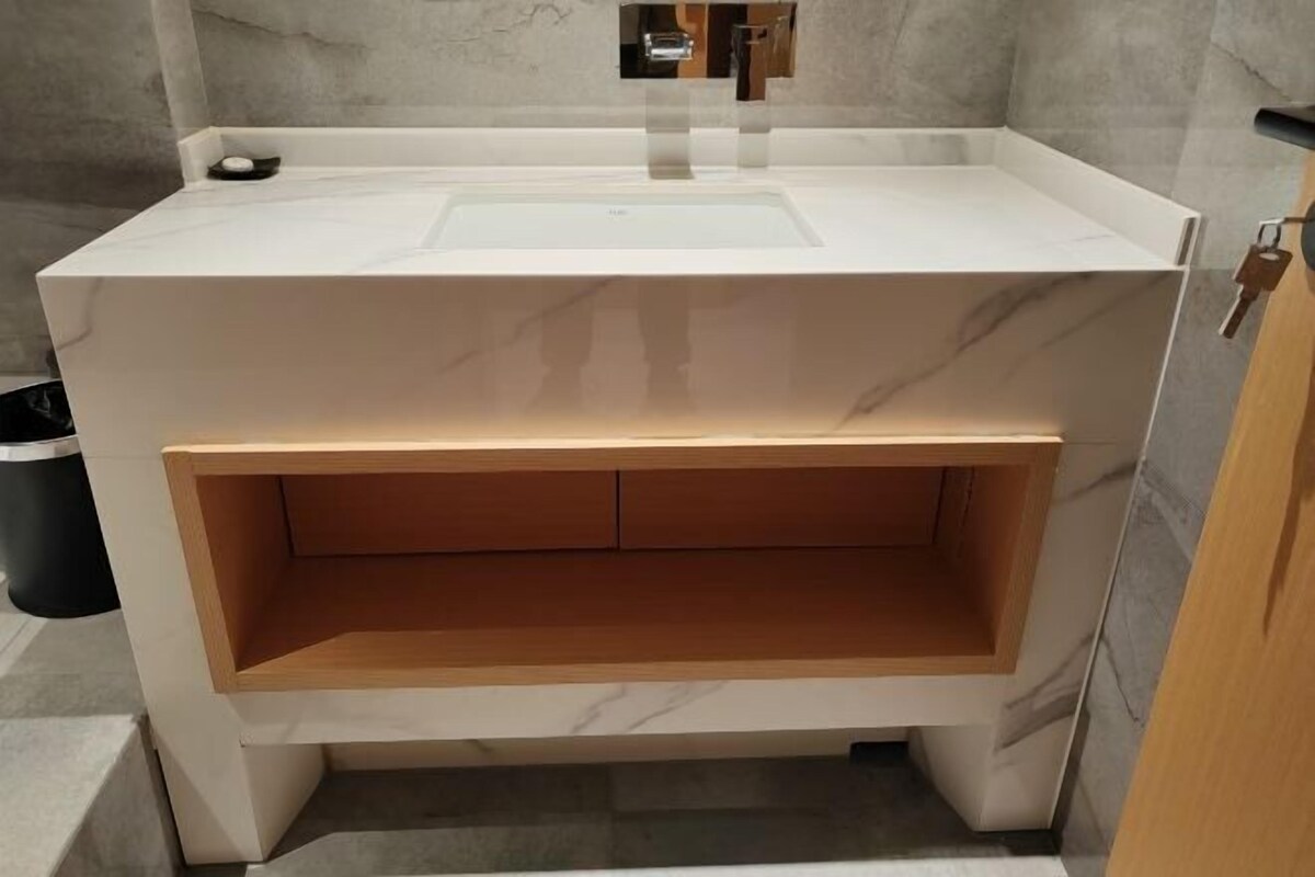 Une salle de bain avec un lavabo en marbre blanc, un meuble-lavabo en bois et une poubelle.