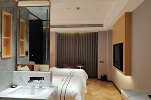 Une chambre d’hôtel avec un grand miroir, un lit, une table de chevet, un téléviseur fixé au mur et une fenêtre avec des rideaux.