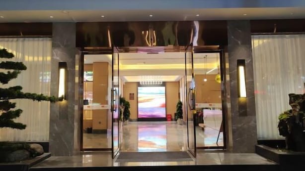 A hotel entrance with a glass door, a reception desk, and a digital display.