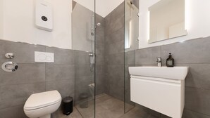 Een moderne badkamer met toilet, een douche met glazen wand, wastafel en spiegel.
