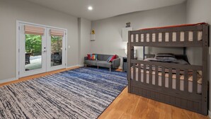 A bedroom with a bunk bed, a sofa, a patterned rug, and a sliding glass door leading to an outdoor area. - Lakefront Roxboro Home w/ Private Dock! (Roxboro)