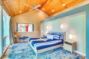 A bedroom with a wooden ceiling, a bed with a blue and white striped bedspread, a nightstand with a lamp, and a view of a room with a red wall and a window. - Lakefront Roxboro Home w/ Private Dock! (Roxboro)