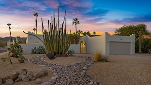 A desert landscape with a white building featuring a large cactus garden and a gravel pathway.