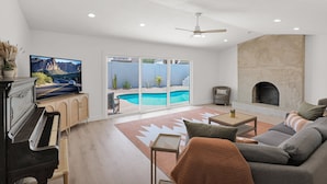 A living room with a piano, a television, a fireplace, and a pool view.
