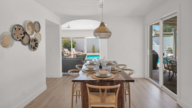A dining area with a wooden table set for six, surrounded by wicker chairs, with a large woven pendant light above.