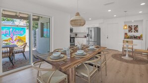 A modern kitchen with white cabinets, a stainless steel refrigerator, and a dining area with a wooden table set for six.