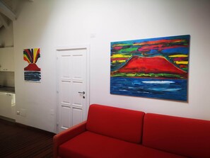 A hallway with a red couch, a white door, and two paintings on the wall.