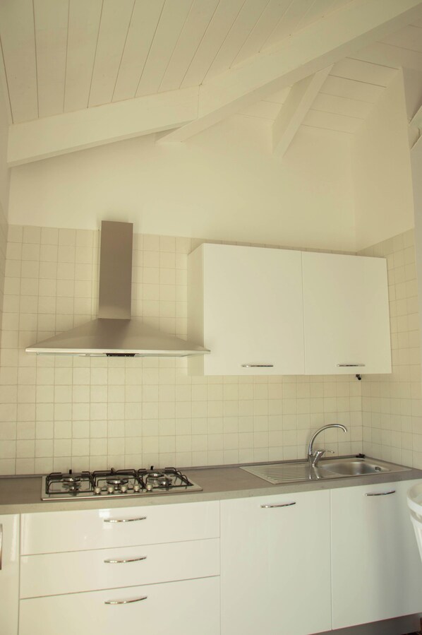 Una cocina con gabinetes blancos, una campana de acero inoxidable, una estufa a gas y un fregadero.