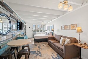 Una habitación acogedora con cama, sofá, mesa de comedor con sillas, un espejo grande y un panel de madera rústico en la pared.