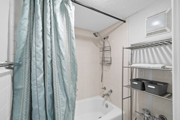 A bathroom with a bathtub, shower, and shelves with storage bins.