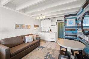 Un espacio habitable compacto con kitchenette, un sofá, una mesa de comedor y una pequeña zona de cocina.