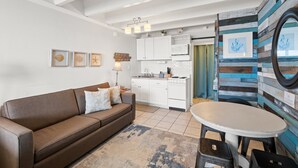 Et moderne køkken med hvide skabe, et spiseområde med et hvidt bord og en brun sofa.
