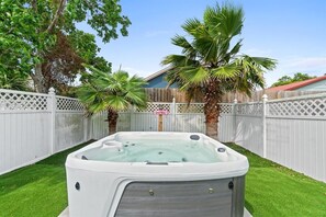 Een hottub in een achtertuin met een houten schutting en palmbomen.
