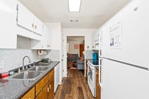 Una cocina compacta con armarios blancos, un lavamanos doble y un refrigerador.