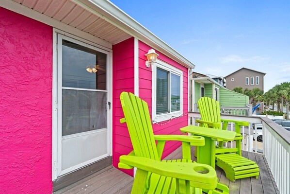 A pink house with a porch, two green chairs, and a window.