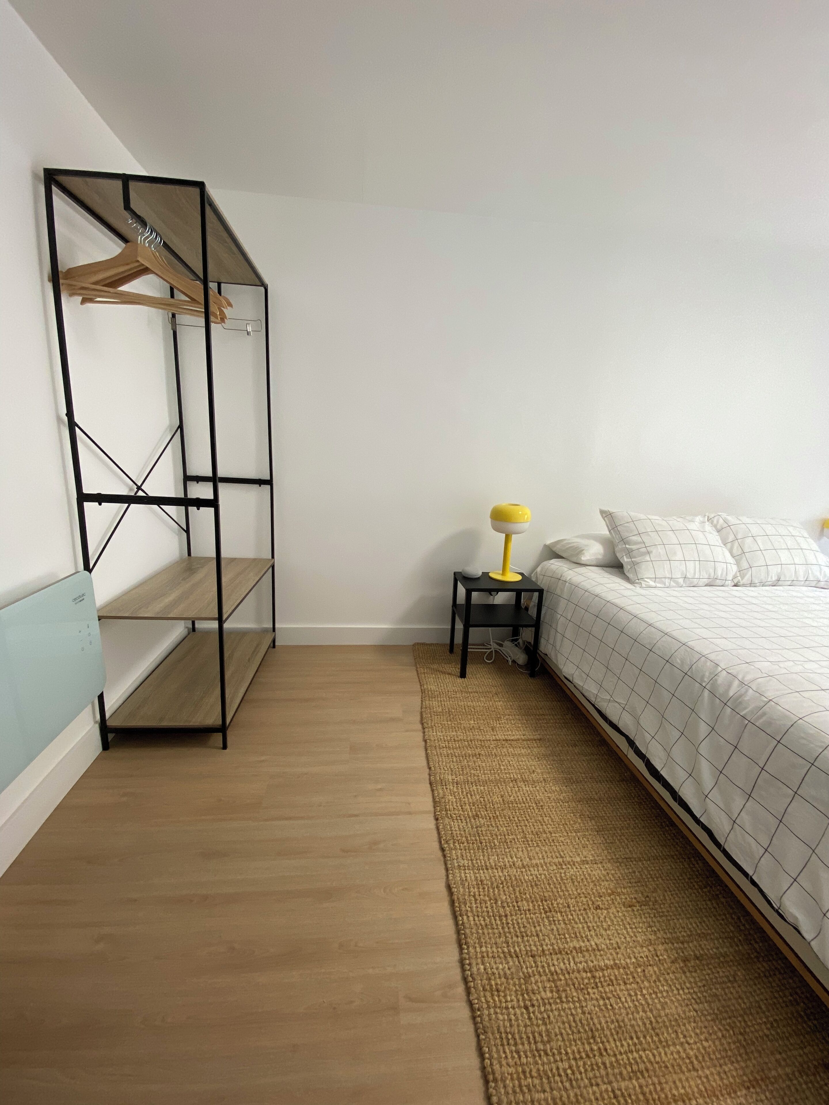 Une chambre à coucher avec un lit, une table de chevet avec une lampe, une étagère suspendue et un plancher en bois.