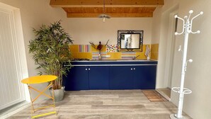 A kitchen with wooden beams, a blue cabinet, a yellow table, and a plant. - La Casa de Babou (Le Château-d'Oléron)