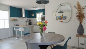 A modern kitchen with teal walls, a dining area with a round table and chairs, and a large mirror on the wall. - La Casa de Babou (Le Château-d'Oléron)