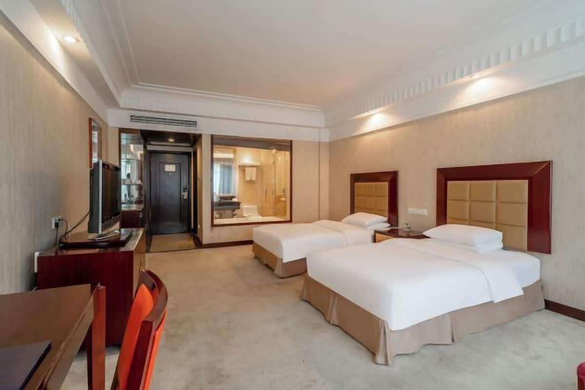 A hotel room with two beds, a desk, a chair, a TV, and a bathroom visible through an open door.