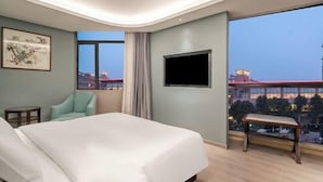 Une chambre d’hôtel avec un grand lit, une télévision, une chaise et une fenêtre donnant sur la ville.