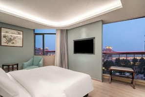A hotel room with a large bed, a television, a chair, and a window with a city view.
