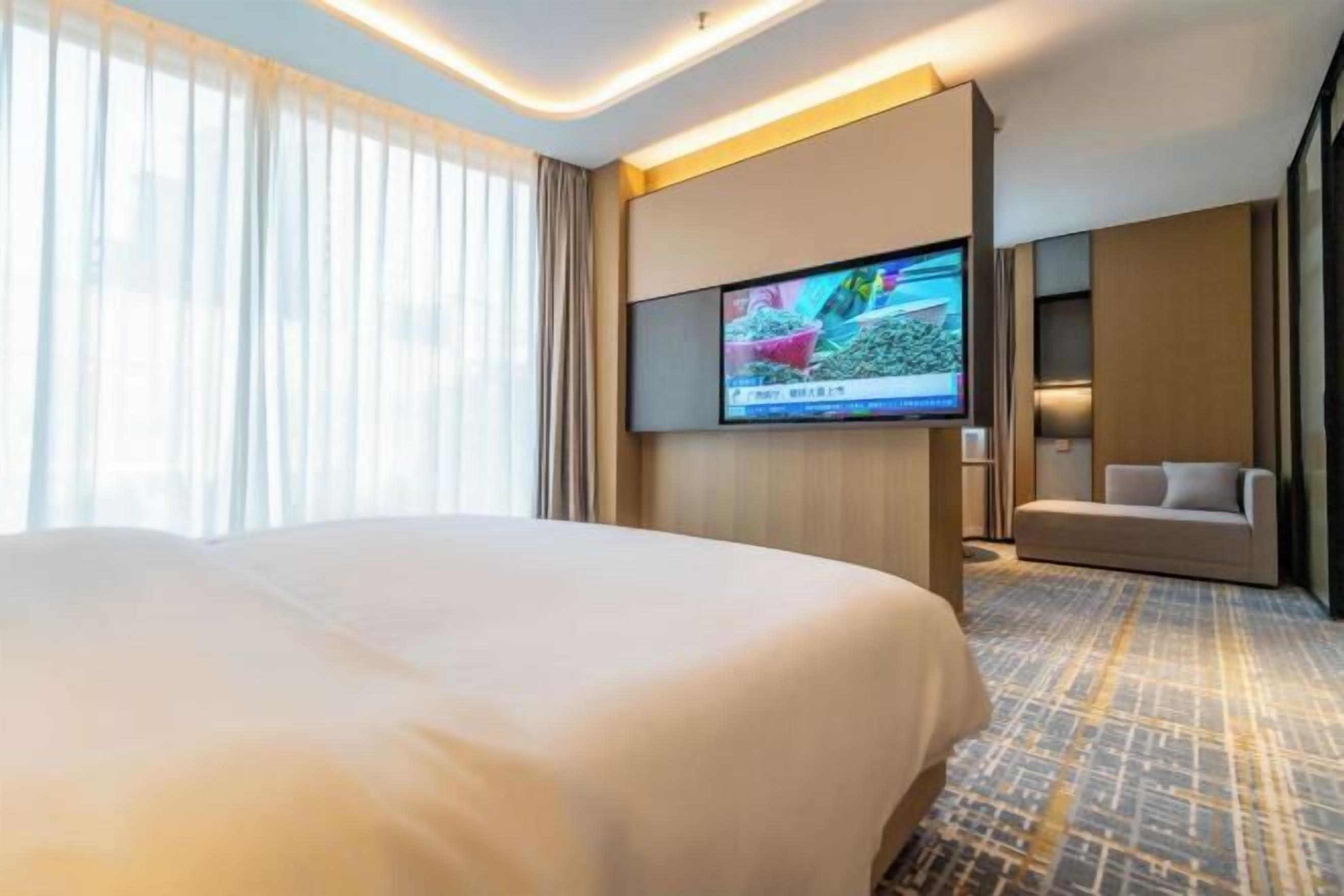 A hotel room with a large bed, a flat-screen TV mounted on the wall, a sofa, and a patterned carpet.