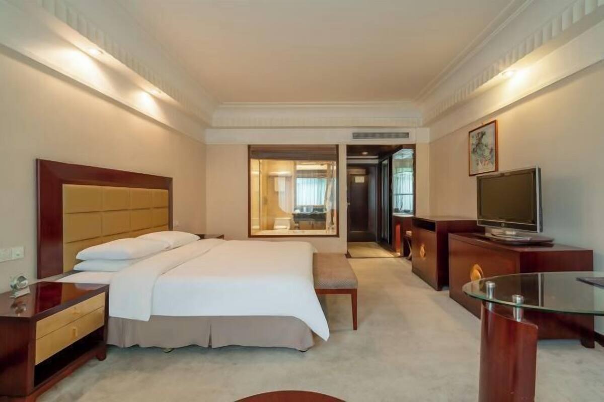 A hotel room with a large bed, a TV, a desk, and a glass coffee table.