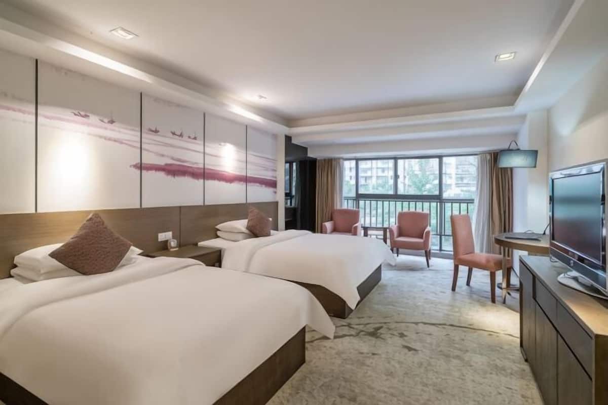 A hotel room with two beds, a TV, a desk, and a balcony with a view.