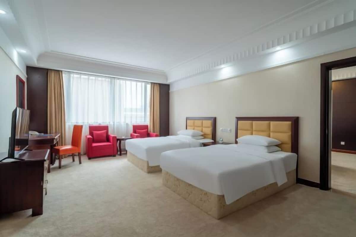 A hotel room with two beds, a desk, a chair, and a TV.