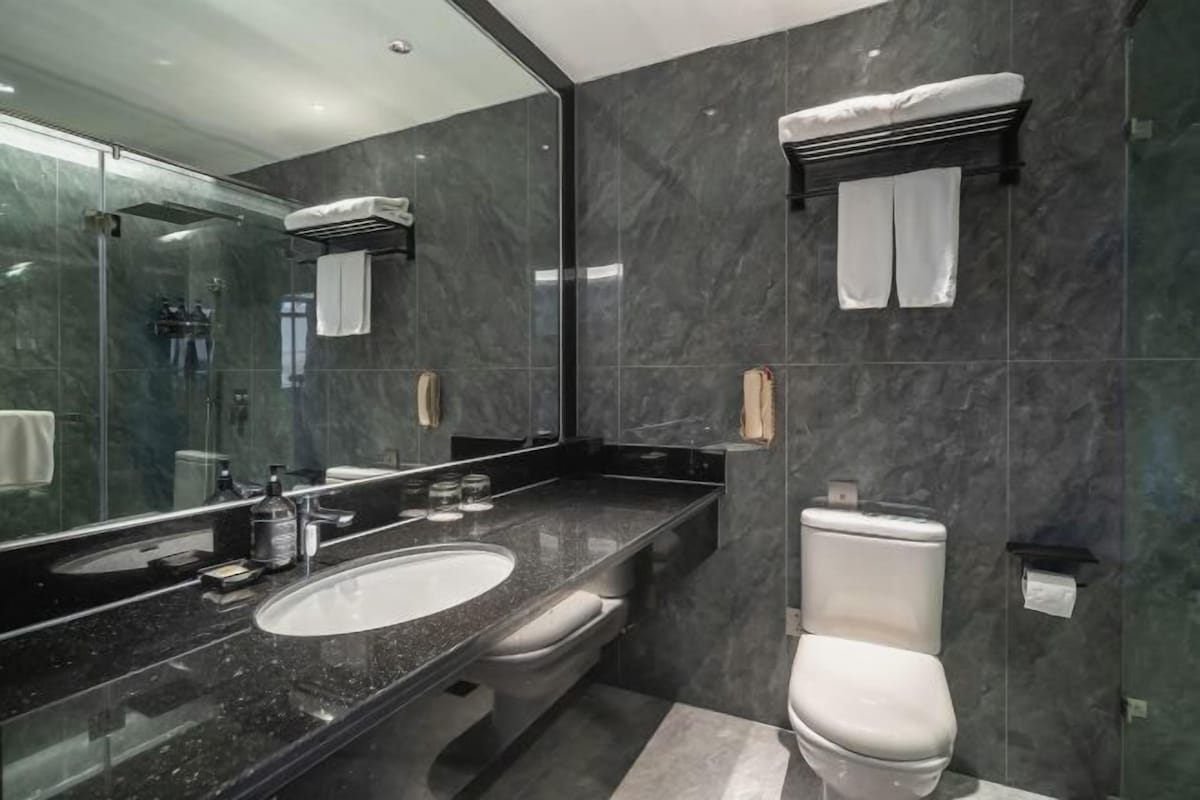A modern bathroom with a large mirror, a sink, a toilet, and a shower area.