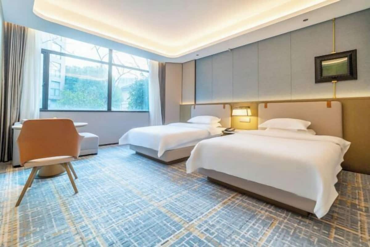 A hotel room with two beds, a desk, and a chair.