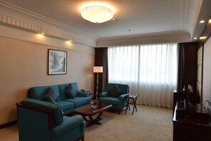 A hotel room with a teal sofa set, a small table, a lamp, and a television.