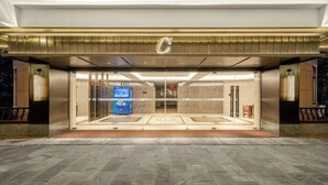 L'entrée d'un hôtel au design moderne, avec un logo en forme de « C » bien visible, des portes en verre et un espace d'accueil doté d'un comptoir bleu.